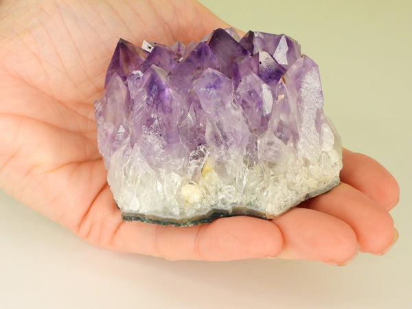 Beautiful Amethyst cluster with inclusions in someone's hand. Front view, close up