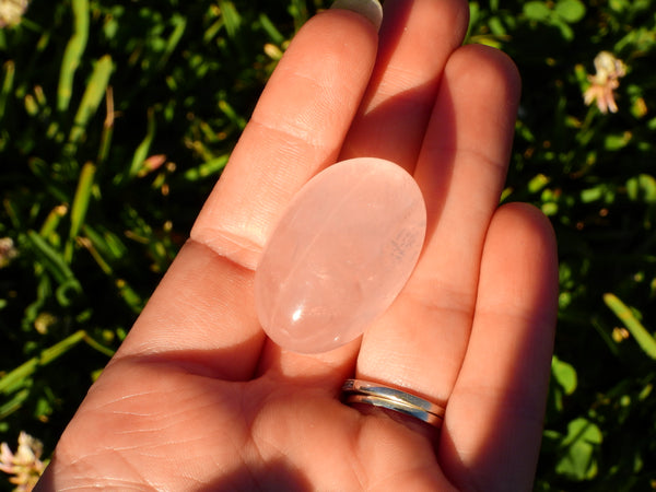 One single high quality Rose Quartz pumble sparkling in the sunshine in someone's hand.