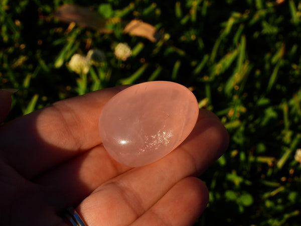 One single high quality Rose Quartz pumble sparkling in the sunshine in someone's hand. Different lighting